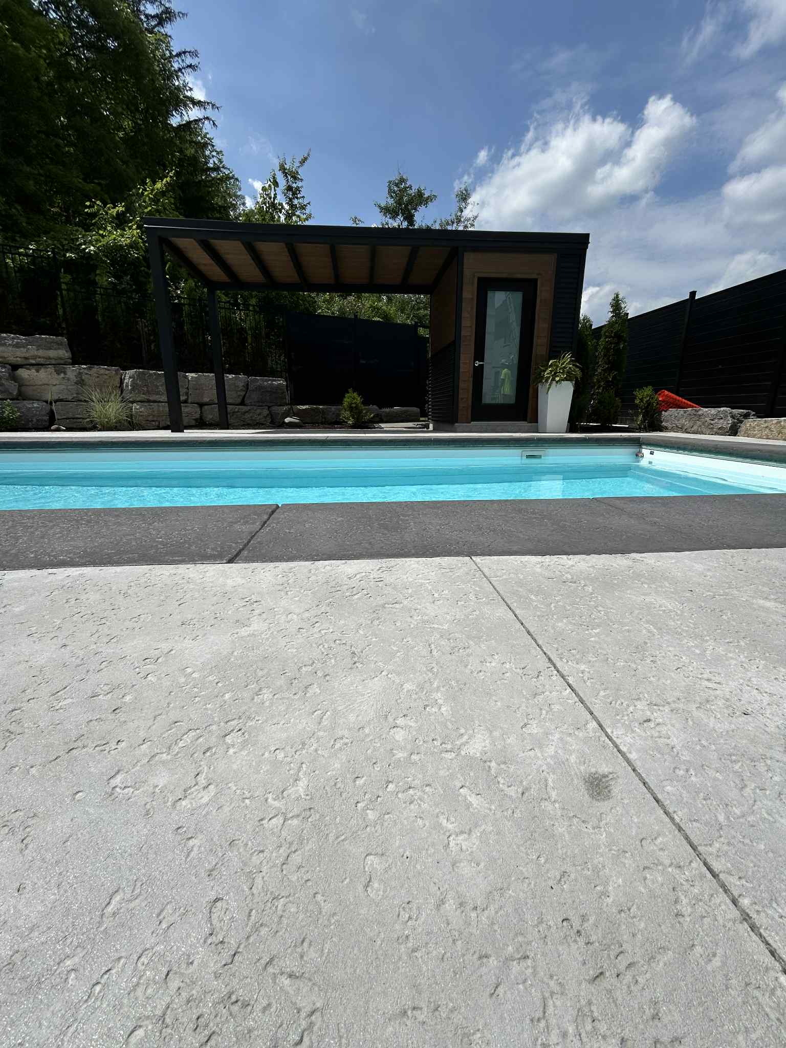 Front view across the pool toward the modern black and wood-look pavilion